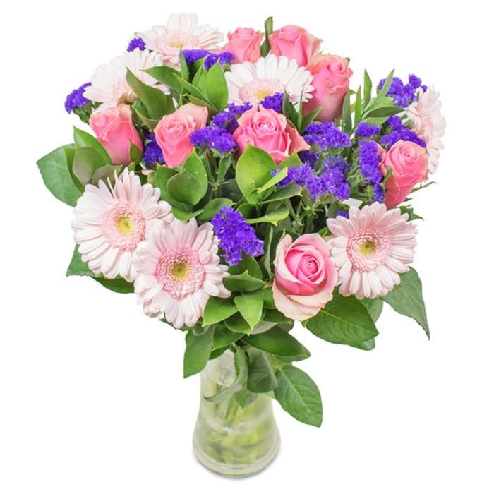A beautifully balanced bouquet embodying the spirit of Teddington, artfully arranged in a crystal-clear vase and set against a crisp white backdrop. Around seven to nine soft pink roses, some tightly budded and others opening gracefully, form the heart of the display. Their classic spiral shapes are echoed by five to seven pale pink gerbera daisies, each with wide, lovely petals and nearly white centers, recalling the gentle blooms found in Teddington's riverside gardens. Scattered throughout, bright clusters of violet-purple statice bring a flash of modern vibrancy while adding rich texture. The lush green foliage is deep and abundant, reminiscent of the leafy expanses of Bushy Park nearby, lending freshness and volume. With visible stems and sparkling water in the vase, the arrangement promises just-picked quality and the hallmark freshness of local delivery. Suitable for birthdays, anniversaries, Mother's Day, or as a charming centrepiece for a Teddington home or business, this bouquet expresses joy, celebration, and the caring ethos of Flowers Teddington.