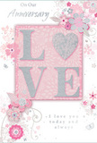 A refined anniversary card is pictured, its design marrying tenderness and sophistication in a way that would feel perfectly at home on a Teddington mantelpiece, perhaps beside a vase of fresh roses. The card's palette is a gentle mix of pearly white, soft grey, and powder pink, creating a serene atmosphere. At the centre, the word LOVE appears in bold, raised letters, their edges traced with a line of glitter that adds just enough sparkle to lift the design without making it flashy. The letters rest on a blush-coloured rectangle that seems to softly glow, providing a warm anchor amid the pale surroundings. Flowing out from this central motif, a delicate spray of illustrated flowers, fine stems, and swirling vines drifts across the card. Each blossom is drawn with careful, refined lines and touched with hints of silver foil, suggesting the meticulous detail of a florist assembling an anniversary bouquet for delivery along Teddington High Street. The vines curve and loop gracefully, giving the composition a feeling of lightness and movement. The background remains mostly white, with faint washes of pink and grey that echo the tones of the flowers while keeping the overall look crisp and airy. Elegant script wording weaves through the design, expressing anniversary blessings in a style that feels both personal and timeless. Taken together, the elements create a card that feels like a softly scented memory captured on paper-perfect as a companion to fresh flowers when celebrating another year of shared stories and quiet moments at home.